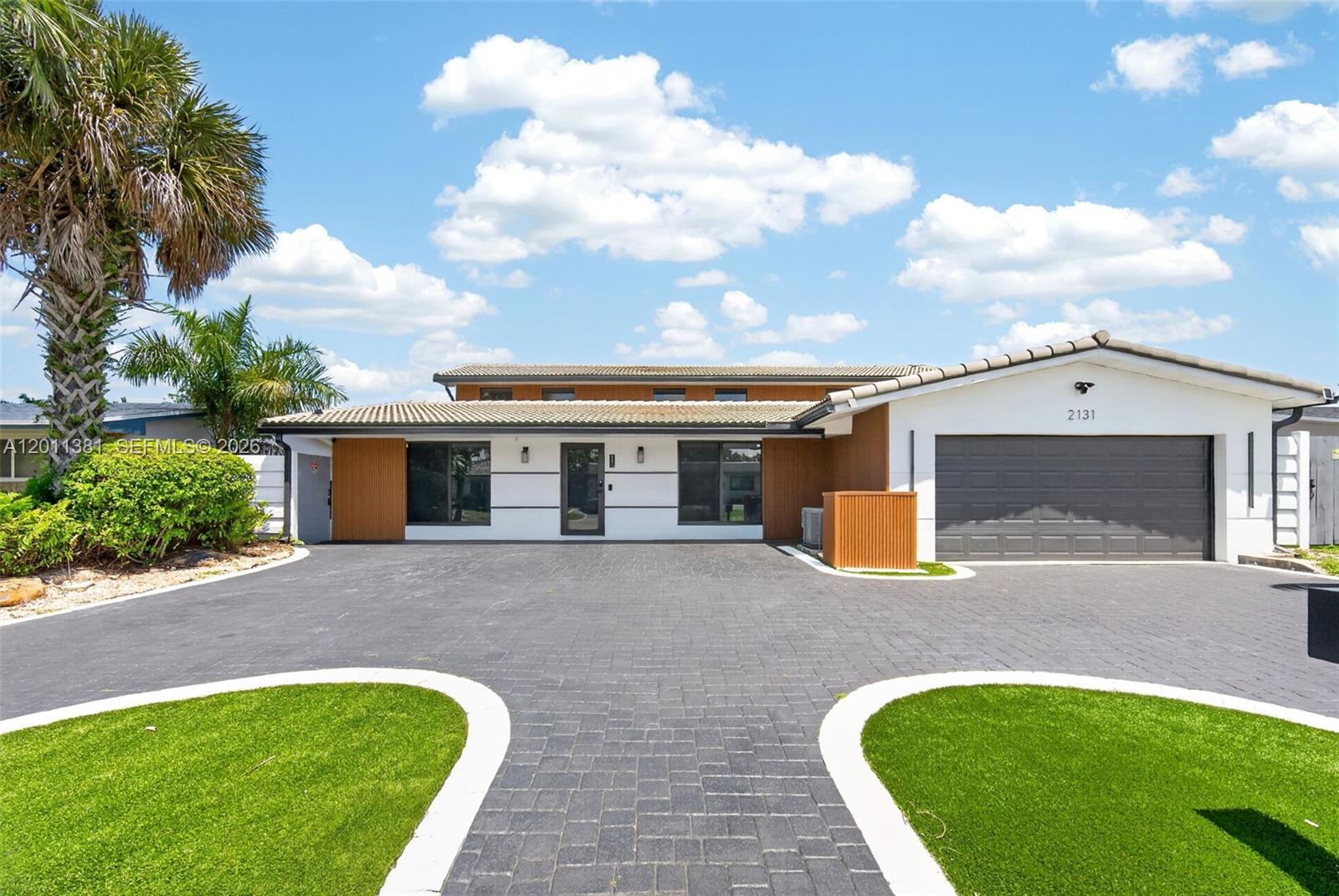 A modern single-story house features a paved driveway, white walls, wood accents, and a garage — 2131 N 53rd Ave, Hollywood FL 33021, HOLLYWOOD, FL