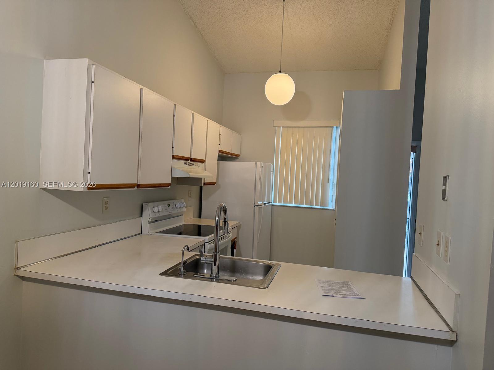 A kitchen features white cabinets, white appliances, a stainless steel sink, and a pendant light — 6725 NW 188th Ter, Hialeah FL 33015, HIALEAH, FL