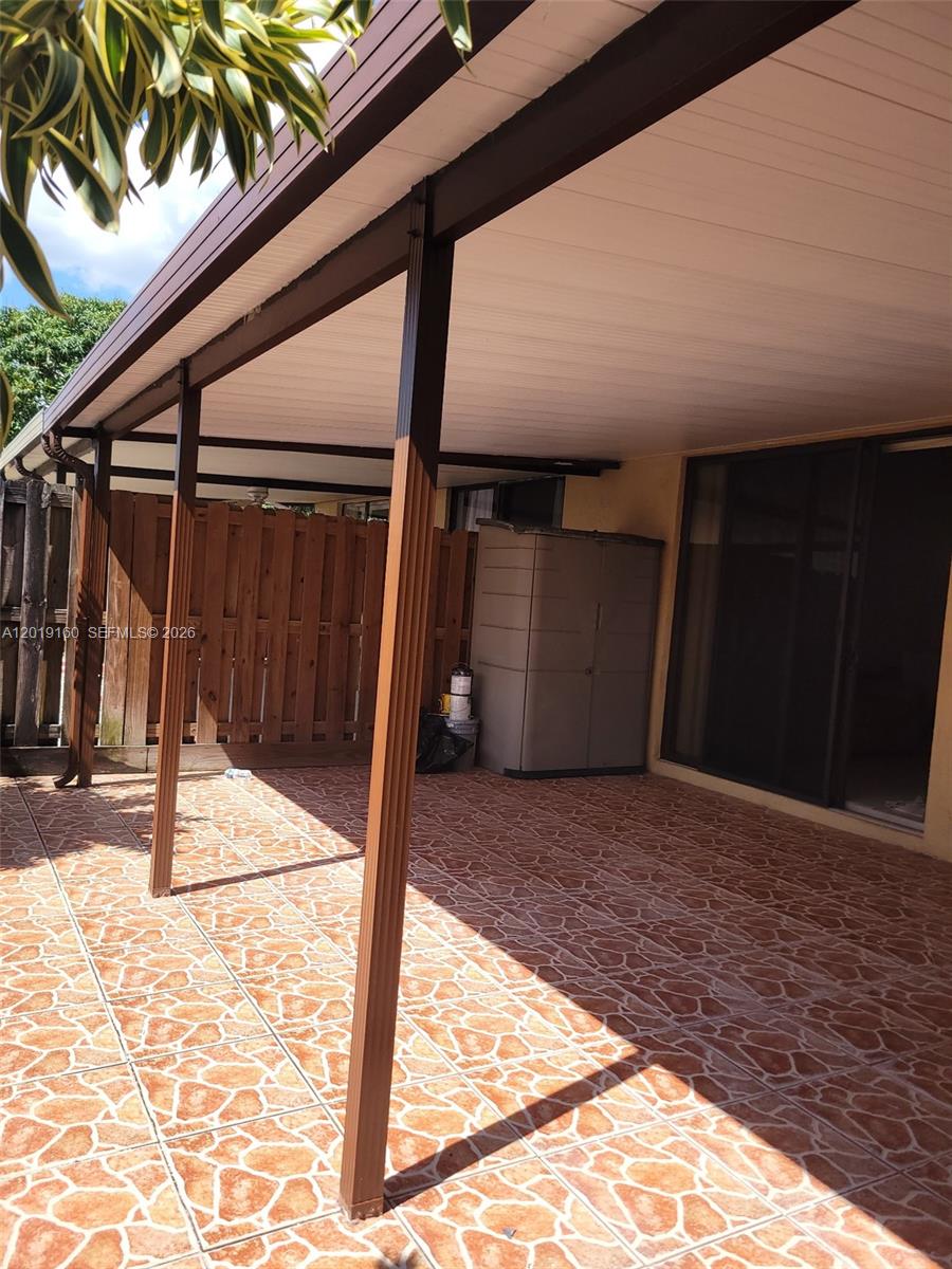A covered patio features tiled flooring, brown support posts, and a wooden privacy fence — 6725 NW 188th Ter, Hialeah FL 33015, HIALEAH, FL