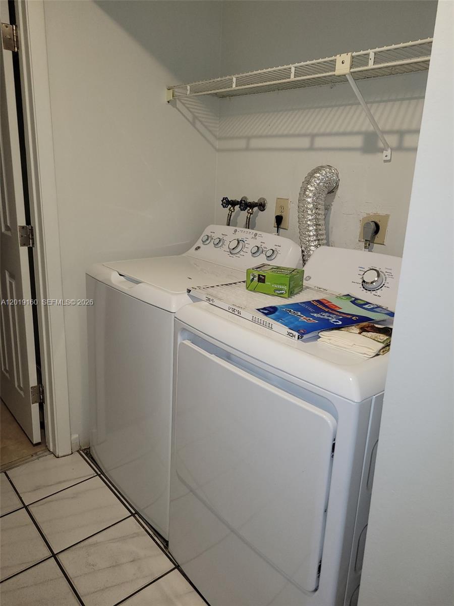 A laundry closet features a white washer and dryer with a wire shelf above — 6725 NW 188th Ter, Hialeah FL 33015, HIALEAH, FL