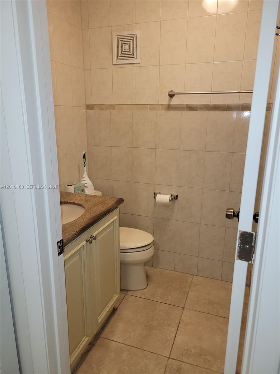 A small bathroom features a vanity with a stone countertop, a toilet, and tiled walls — 6725 NW 188th Ter, Hialeah FL 33015, HIALEAH, FL