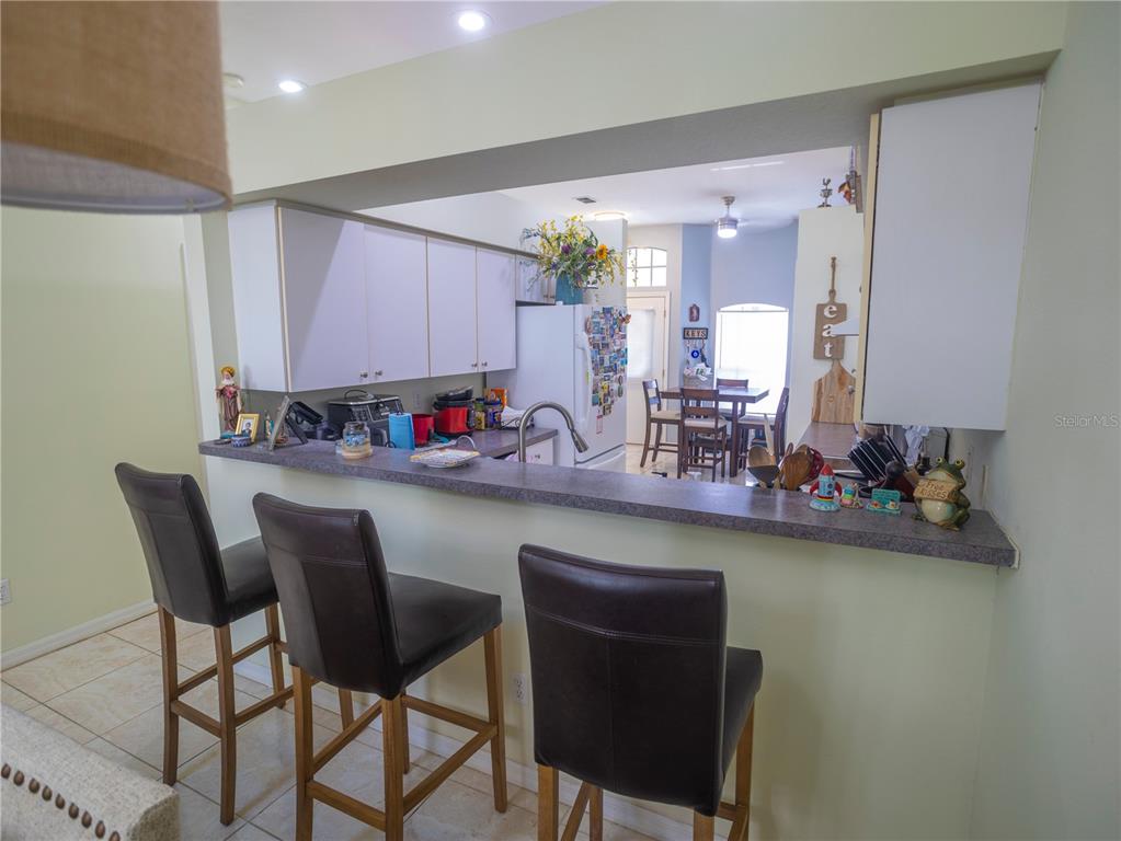 A kitchen with a breakfast bar, dark leather stools, and white cabinets overlooks a dining area — 12537 HOLLYBROOK LANE, HUDSON, FL