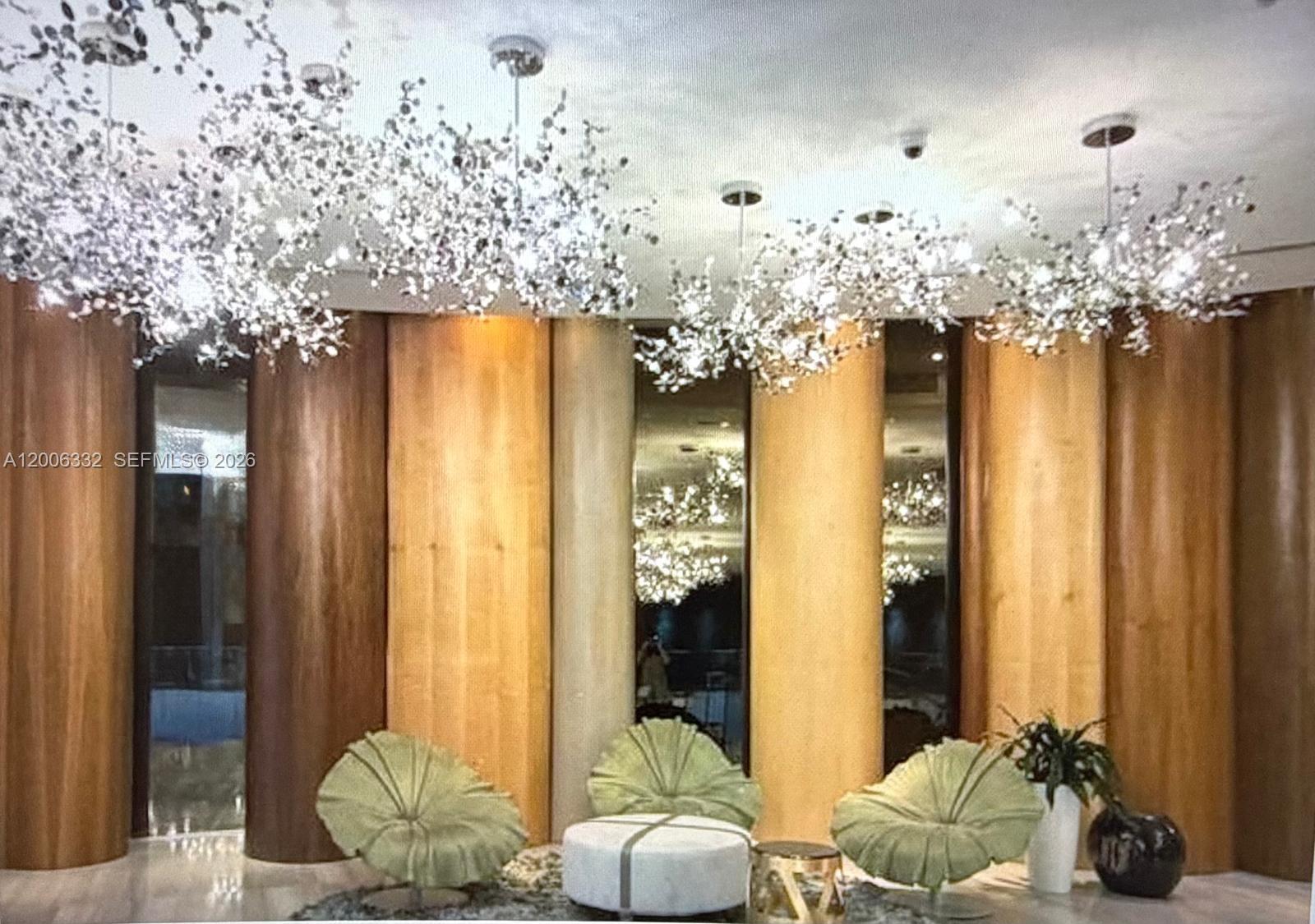 A modern lobby features three sculptural chandeliers, wood-paneled walls, and green petal-shaped chairs — MIAMI, FL