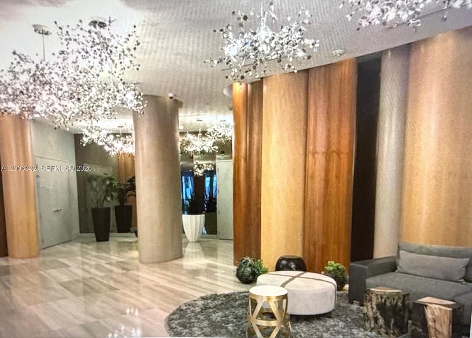 A modern lobby features marble floors, wood-paneled walls, decorative crystal chandeliers, and a seating area — MIAMI, FL