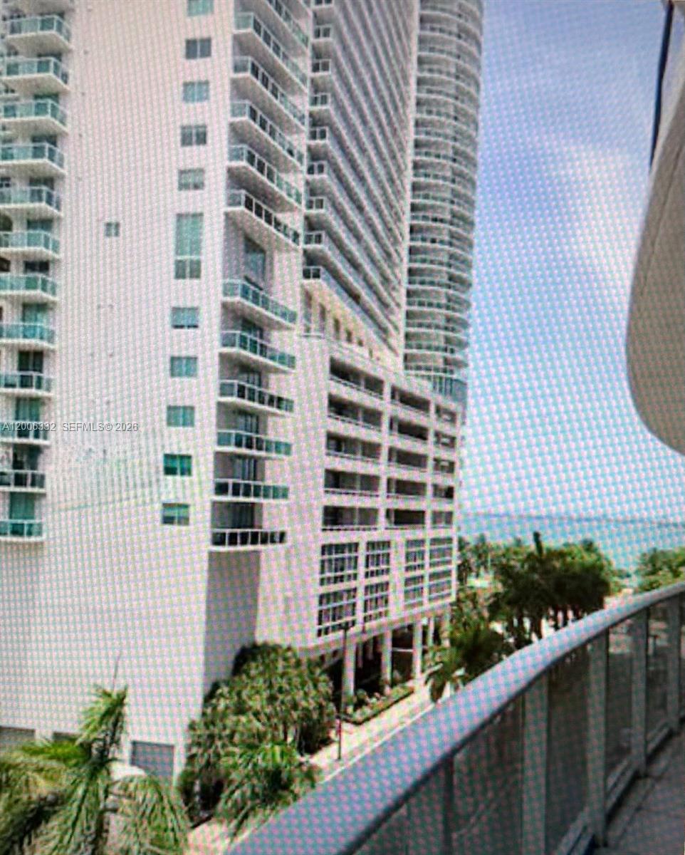 A view from a balcony looking toward a tall white residential high-rise building — MIAMI, FL
