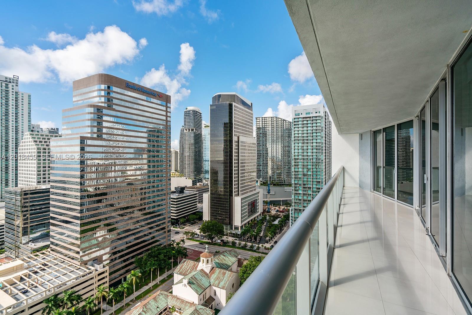 A high-rise balcony with a glass railing overlooks a dense city skyline and a church — 495 Brickell Ave # 2703, Miami FL 33131, MIAMI, FL