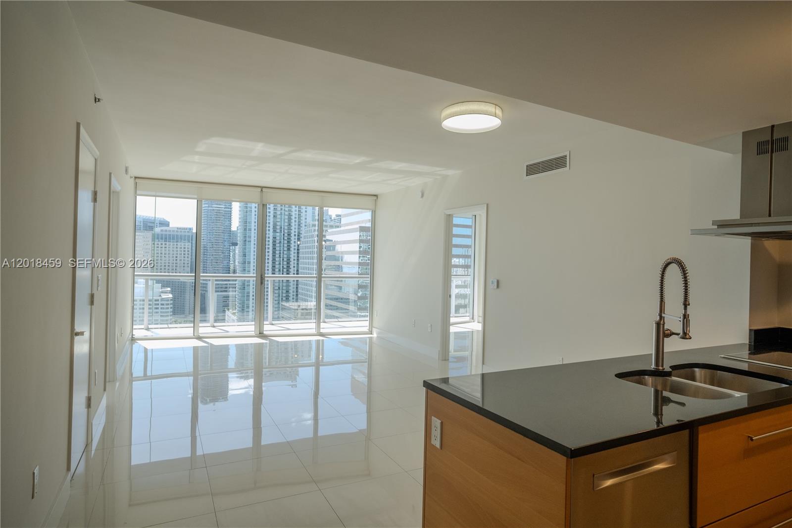 A modern kitchen with a black countertop overlooks a bright living area with floor-to-ceiling windows — 495 Brickell Ave # 2703, Miami FL 33131, MIAMI, FL