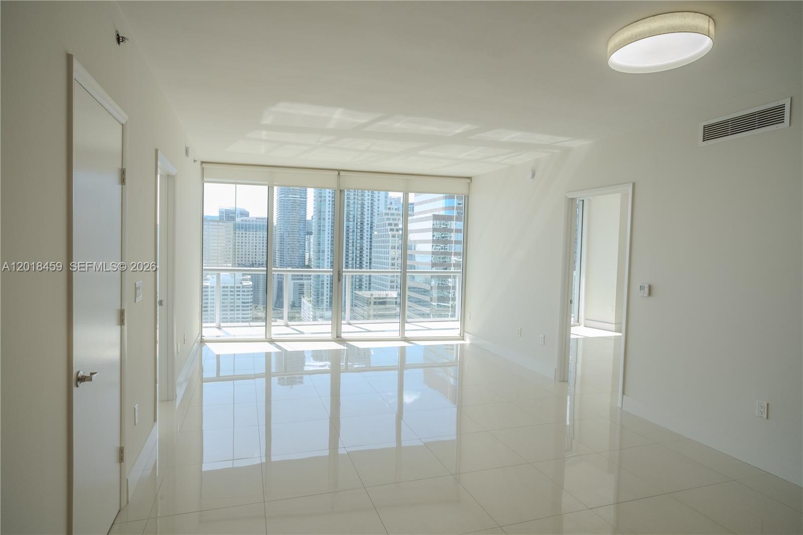 A bright, empty room features white tile floors, floor-to-ceiling windows, and a city view — 495 Brickell Ave # 2703, Miami FL 33131, MIAMI, FL