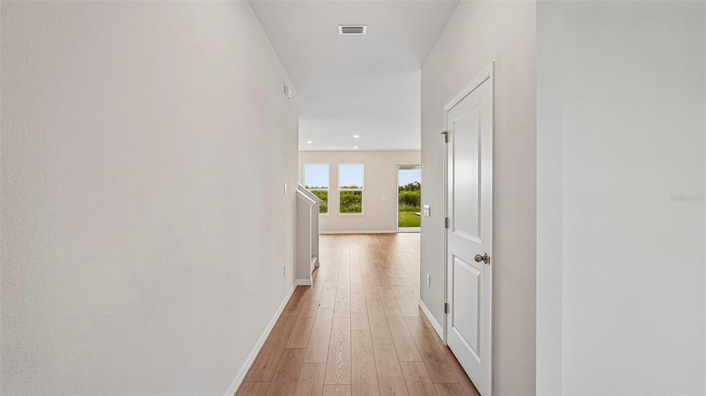 A hallway with light wood flooring leads to an open living area with large windows — 2838 FISHERY COURT, LAKEWOOD RANCH, FL