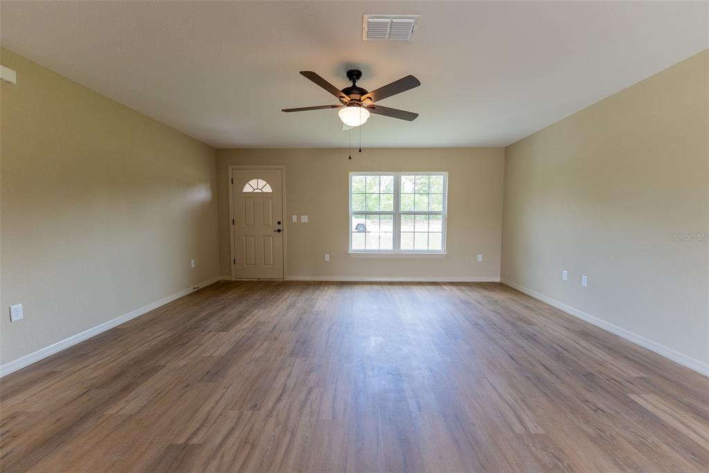 An empty room features light-colored walls, wood-look flooring, a ceiling fan, and a front door — 14787 SW 79TH TERRACE ROAD, OCALA, FL