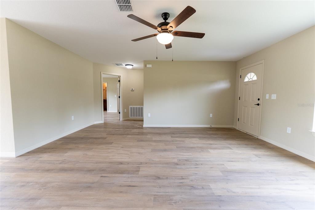An empty living room features light wood-look flooring, beige walls, and a ceiling fan — 14787 SW 79TH TERRACE ROAD, OCALA, FL