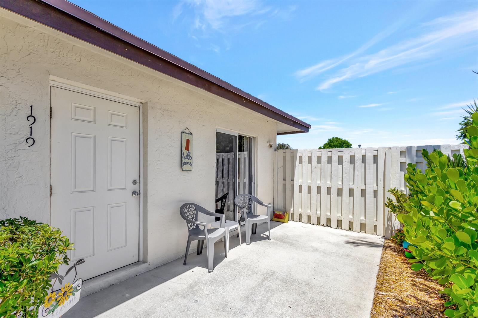 A white stucco exterior features a front door, sliding glass doors, and a small patio — 1919 Doffer Lane, FL 33408, FL