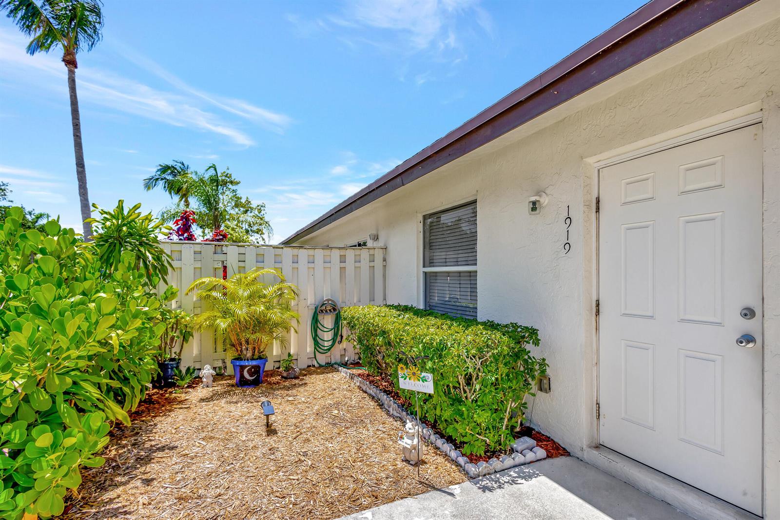 A white exterior wall with a door, a window, and a small landscaped garden area — 1919 Doffer Lane, FL 33408, FL