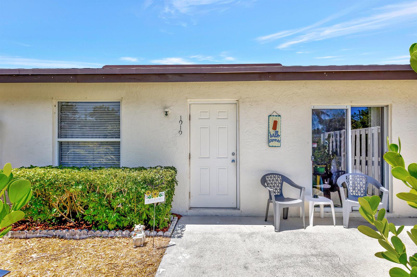 A white exterior wall features a front door, a window, and a small patio area — 1919 Doffer Lane, FL 33408, FL
