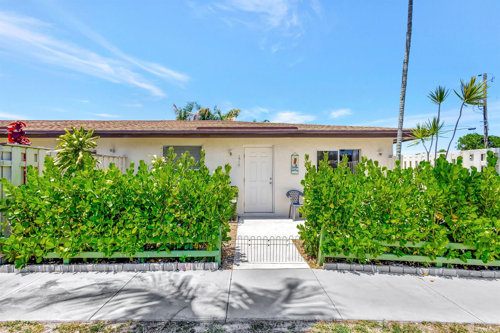 A single-story house exterior features a white door, green hedges, and a small metal gate — 1919 Doffer Lane, FL 33408, FL
