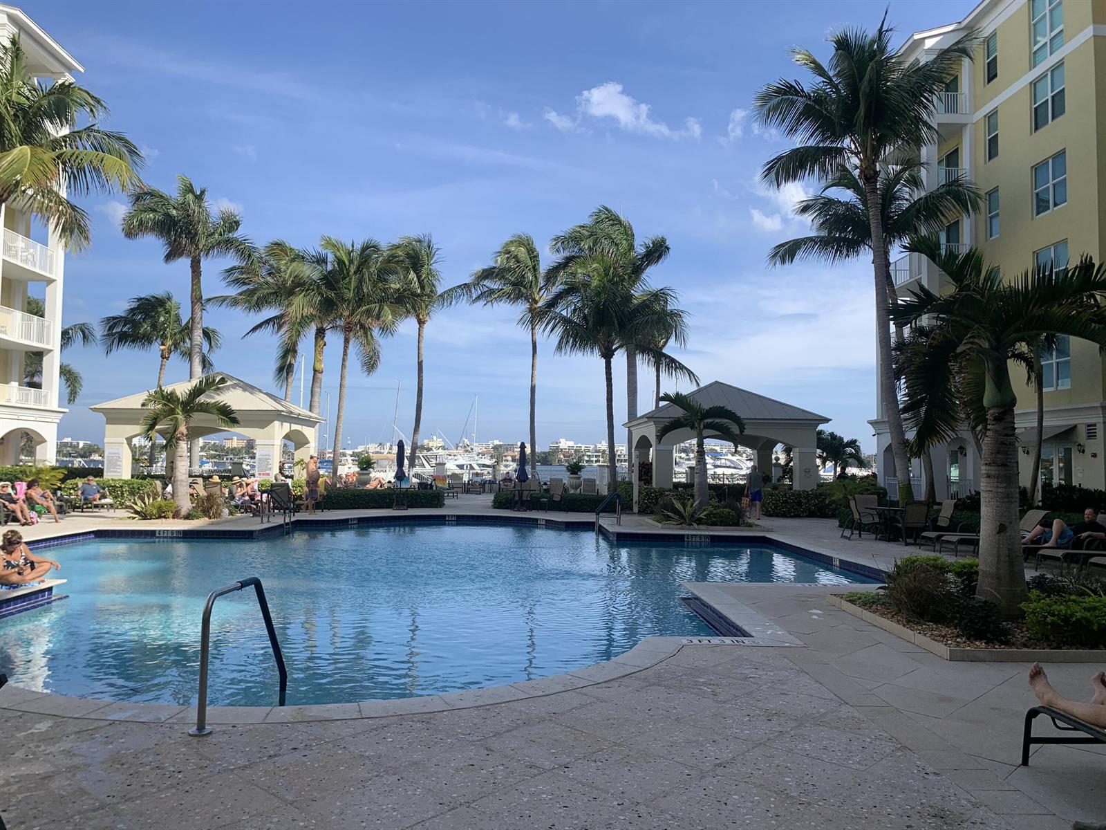 A swimming pool sits between two apartment buildings with palm trees and a marina view — 806 E Windward Way # 111, Lantana FL 33462, LANTANA, FL