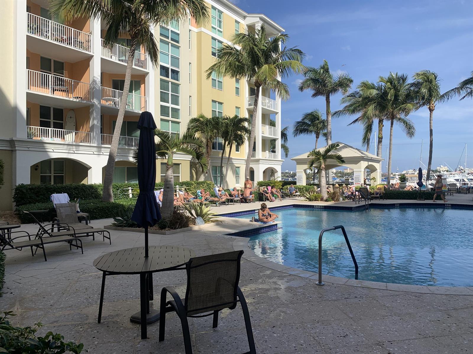 A swimming pool area with lounge chairs, palm trees, and a multi-story building in the background — 806 E Windward Way # 111, Lantana FL 33462, LANTANA, FL