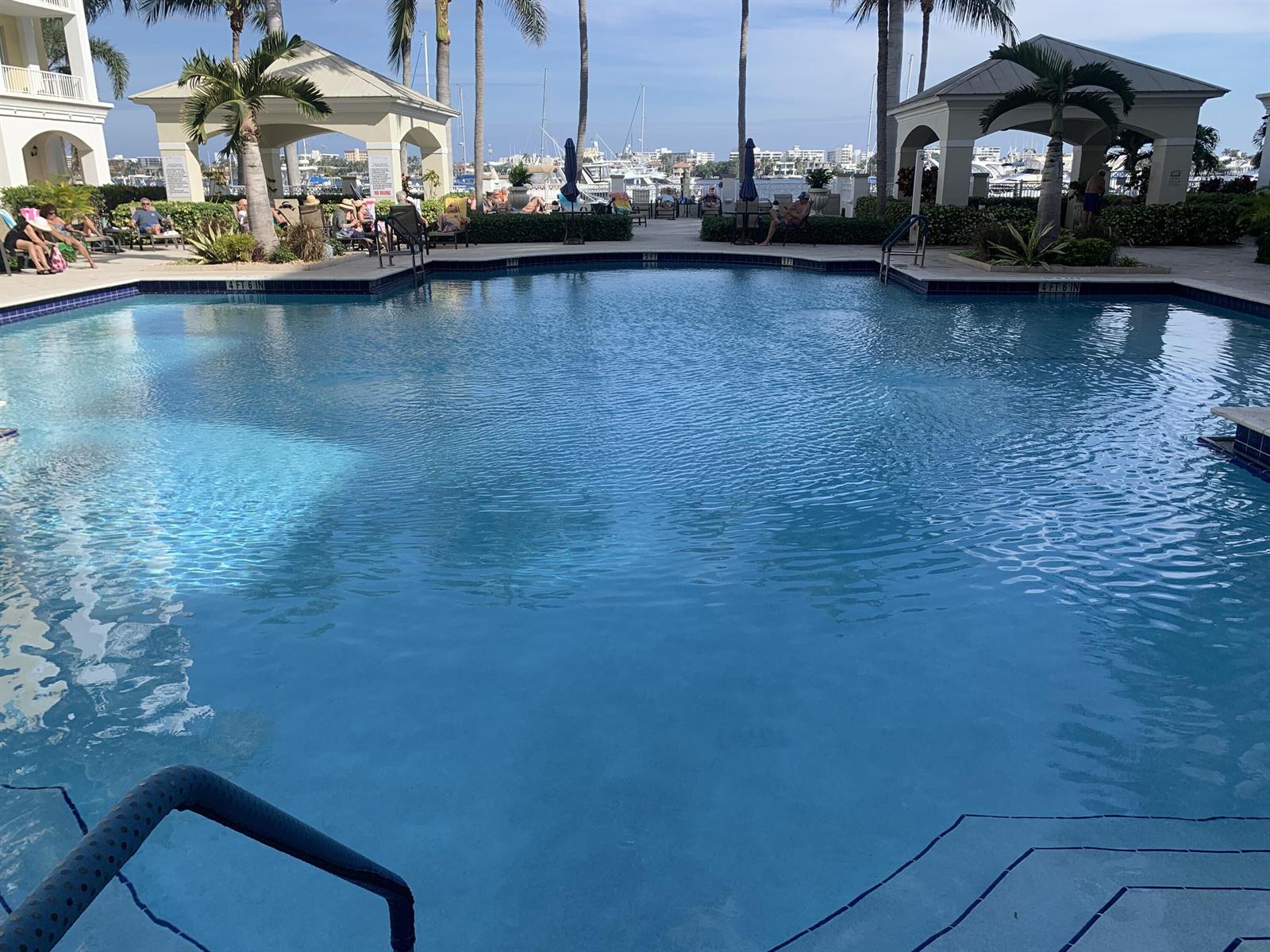 A swimming pool with blue water sits in front of two gazebos and a marina — 806 E Windward Way # 111, Lantana FL 33462, LANTANA, FL