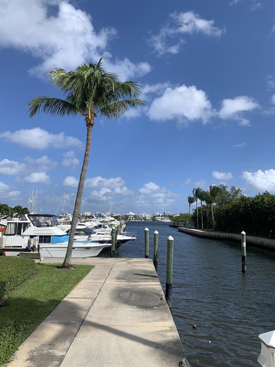 A concrete dock with wooden pilings sits beside a canal lined with boats and palms — 806 E Windward Way # 111, Lantana FL 33462, LANTANA, FL