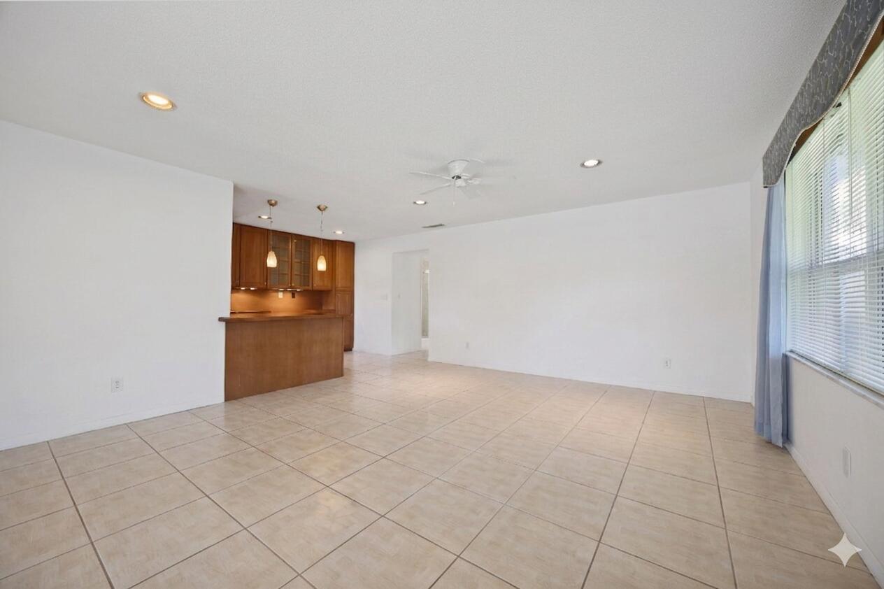 An open-concept living area features light tile flooring, white walls, and a wooden kitchen bar — 275 High Point Court # D, Boynton Beach FL 33435, BOYNTON BEACH, FL