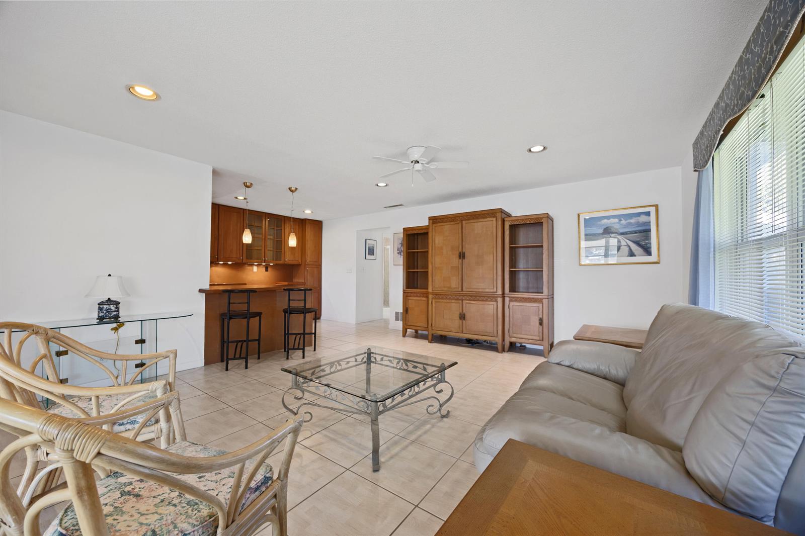 A living room with tile flooring, a glass coffee table, rattan chairs, and a bar area — 275 High Point Court # D, Boynton Beach FL 33435, BOYNTON BEACH, FL