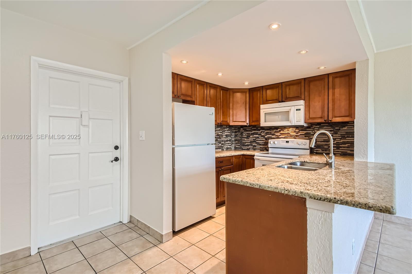 A kitchen features wood cabinets, granite countertops, a white refrigerator, and a tiled floor — 1855 Plunkett St # 406, Hollywood FL 33020, HOLLYWOOD, FL
