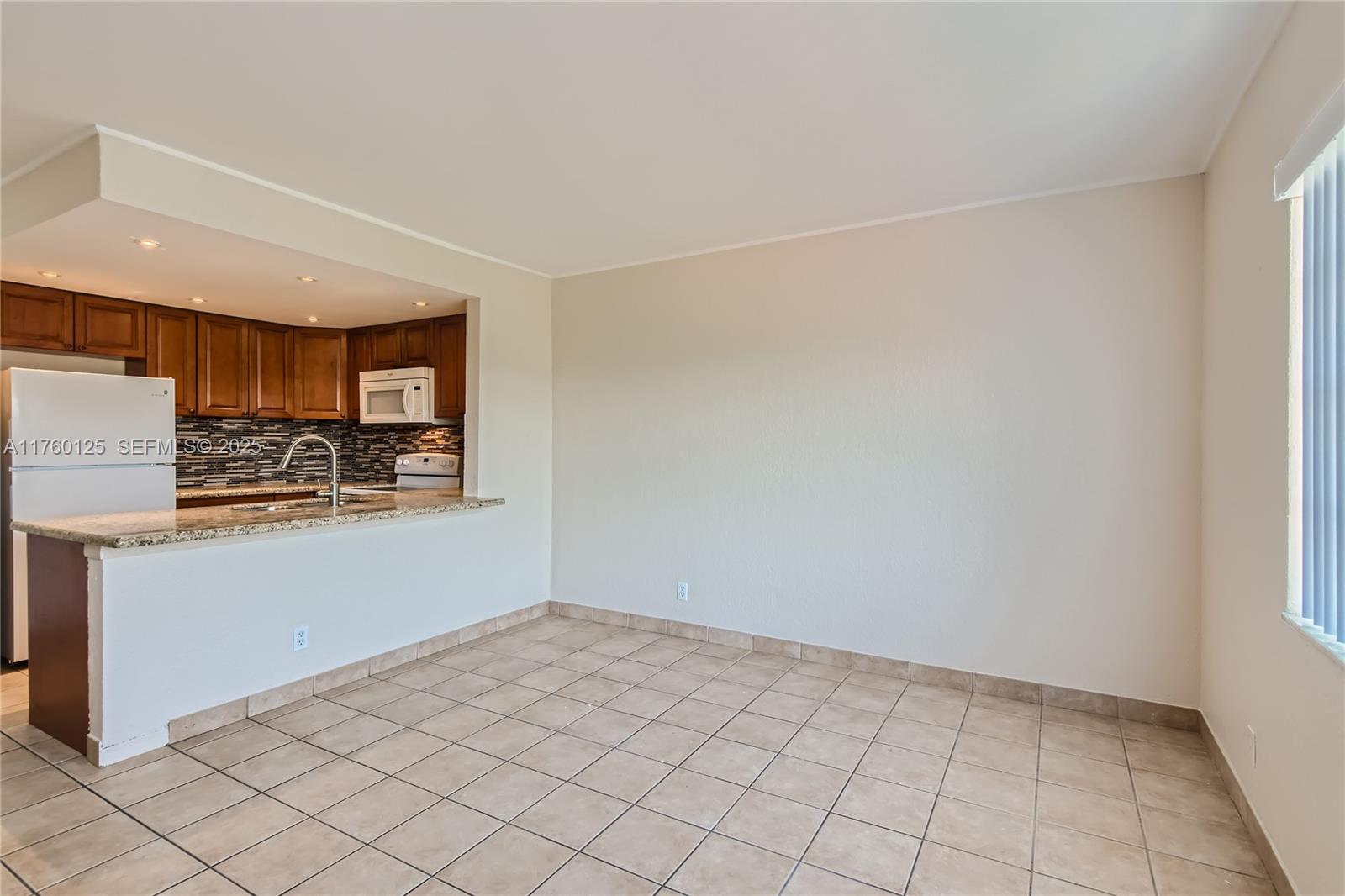An empty dining area with tile flooring sits adjacent to an open kitchen with cabinetry — 1855 Plunkett St # 406, Hollywood FL 33020, HOLLYWOOD, FL