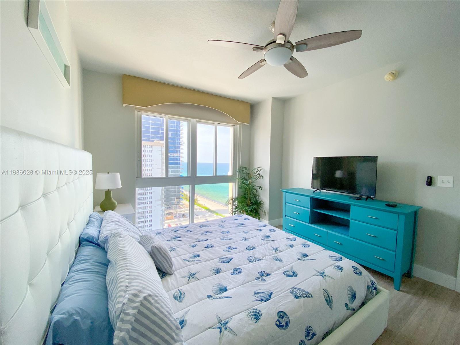 A bedroom with a white tufted headboard, blue dresser, and a view of the ocean — 2080 S Ocean Dr, Hallandale Beach FL 33009, HALLANDALE BEACH, FL