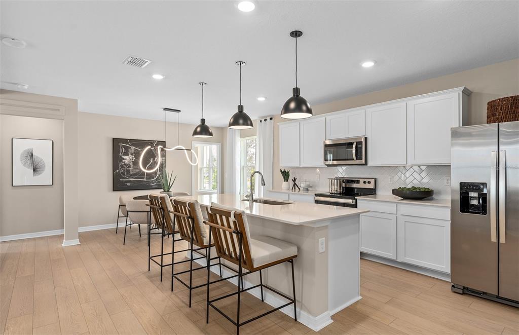 A modern kitchen features white cabinets, a central island with bar seating, and pendant lighting — 4697 SUNNY CITRUS LANE, CLERMONT, FL