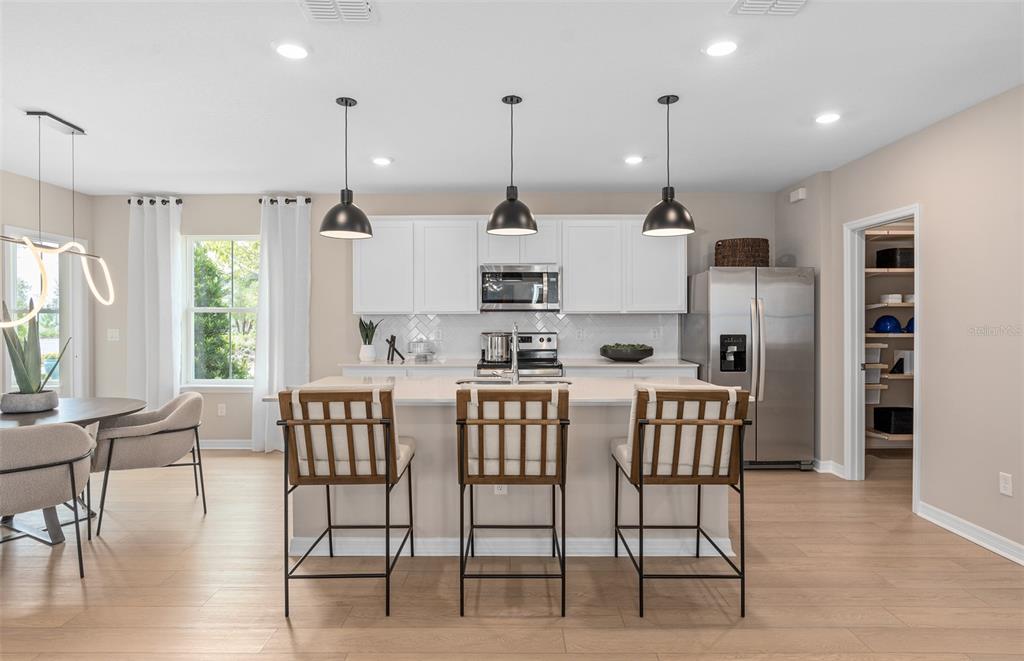 A modern kitchen features white cabinets, a central island with three stools, and stainless appliances — 4697 SUNNY CITRUS LANE, CLERMONT, FL