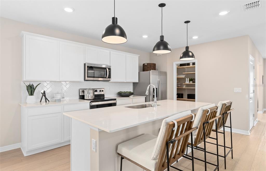 A modern kitchen features white cabinets, a quartz island with bar seating, and pendant lighting — 4697 SUNNY CITRUS LANE, CLERMONT, FL