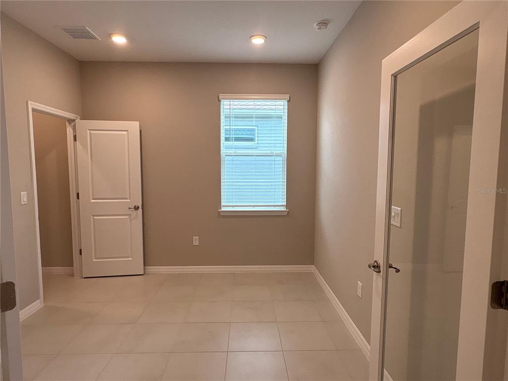 An empty room features beige walls, light-colored tile flooring, a window, and two doorways — 7204 SW 89TH AVENUE, OCALA, FL