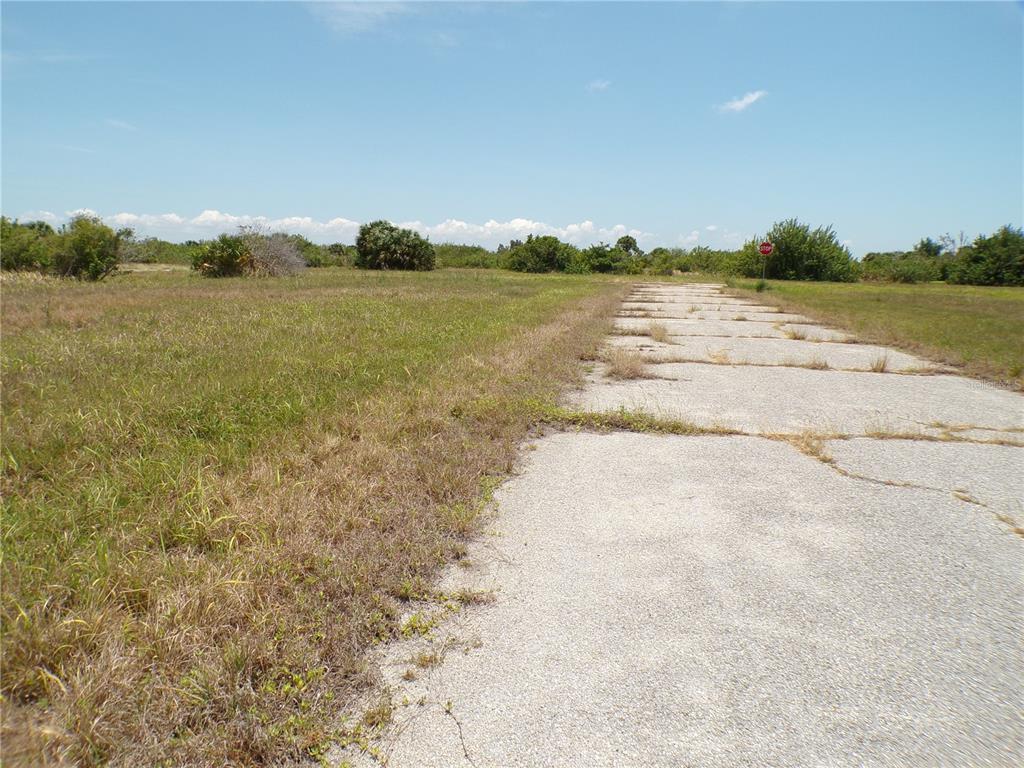 A paved road leads through a grassy, undeveloped lot under a clear blue sky — 13222 PORGY WAY, PLACIDA, FL