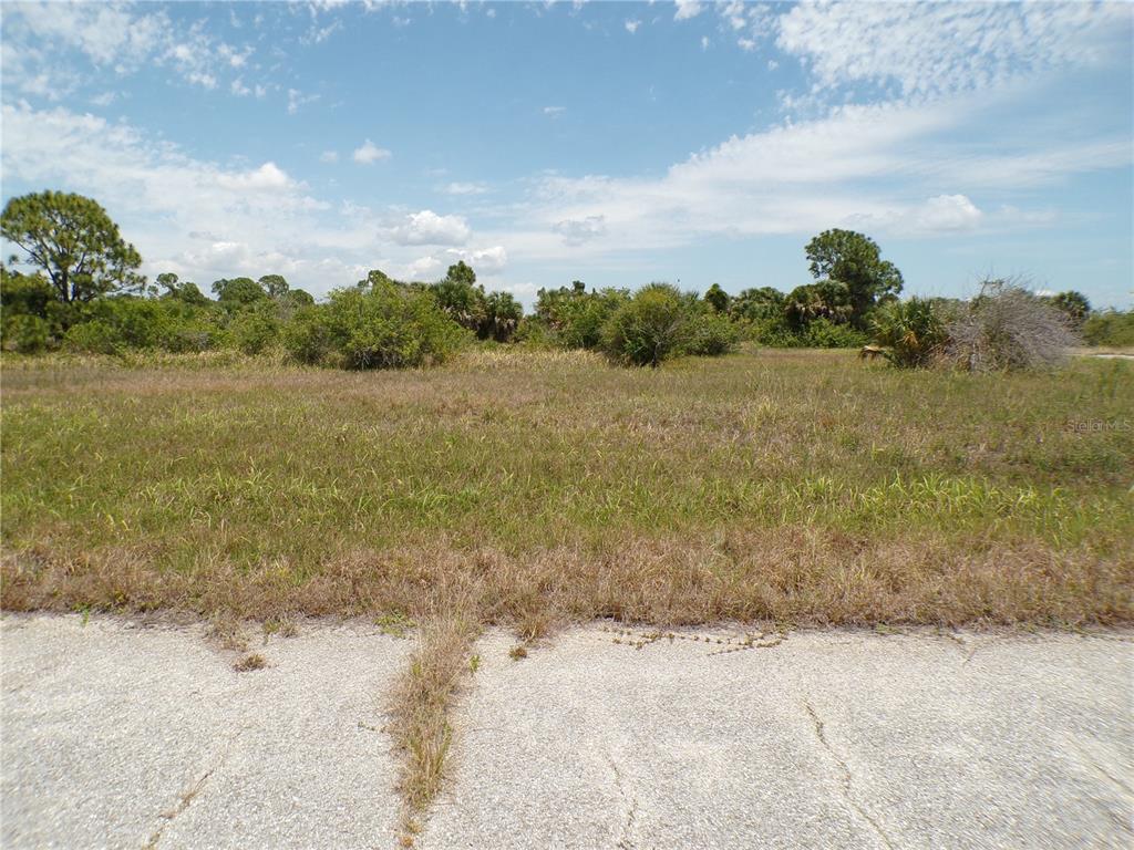 A vacant, grassy lot sits behind a cracked asphalt road under a blue sky — 13222 PORGY WAY, PLACIDA, FL
