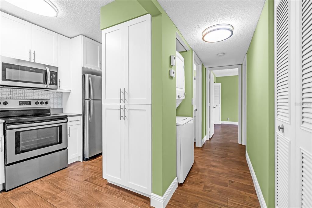 A kitchen with white cabinets and stainless steel appliances leads to a laundry area — 806 SKY PINE WAY UNIT B3, GREEN ACRES, FL