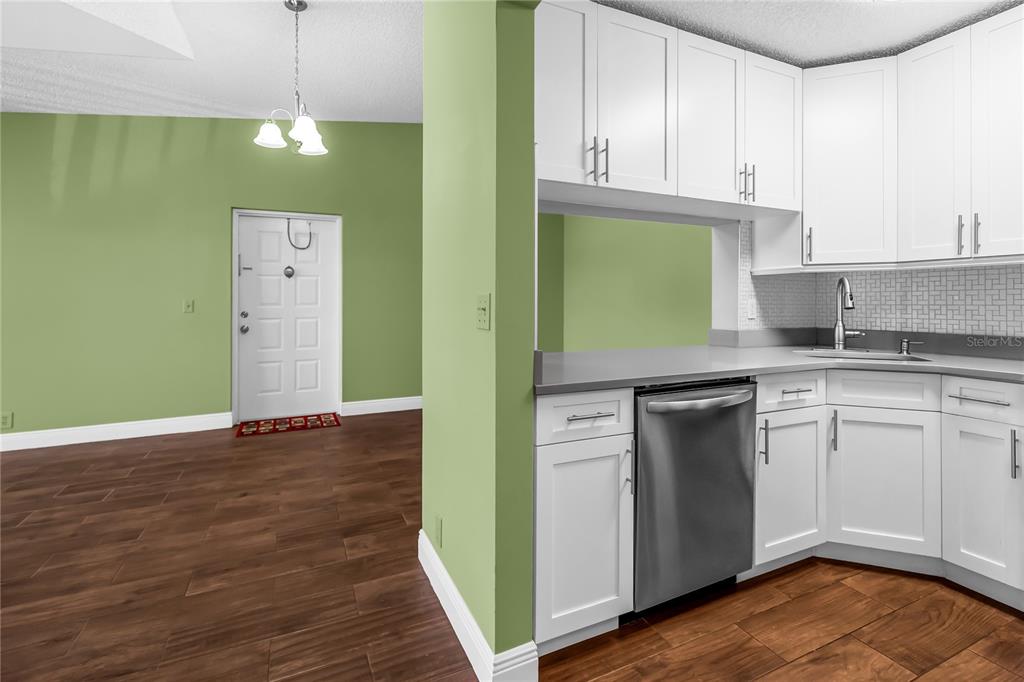 A kitchen with white cabinets and stainless steel appliances opens to a green-walled entryway — 806 SKY PINE WAY UNIT B3, GREEN ACRES, FL