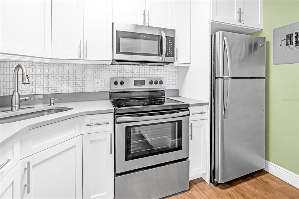 A kitchen features white cabinets, stainless steel appliances, a tiled backsplash, and wood-look flooring — 806 SKY PINE WAY UNIT B3, GREEN ACRES, FL