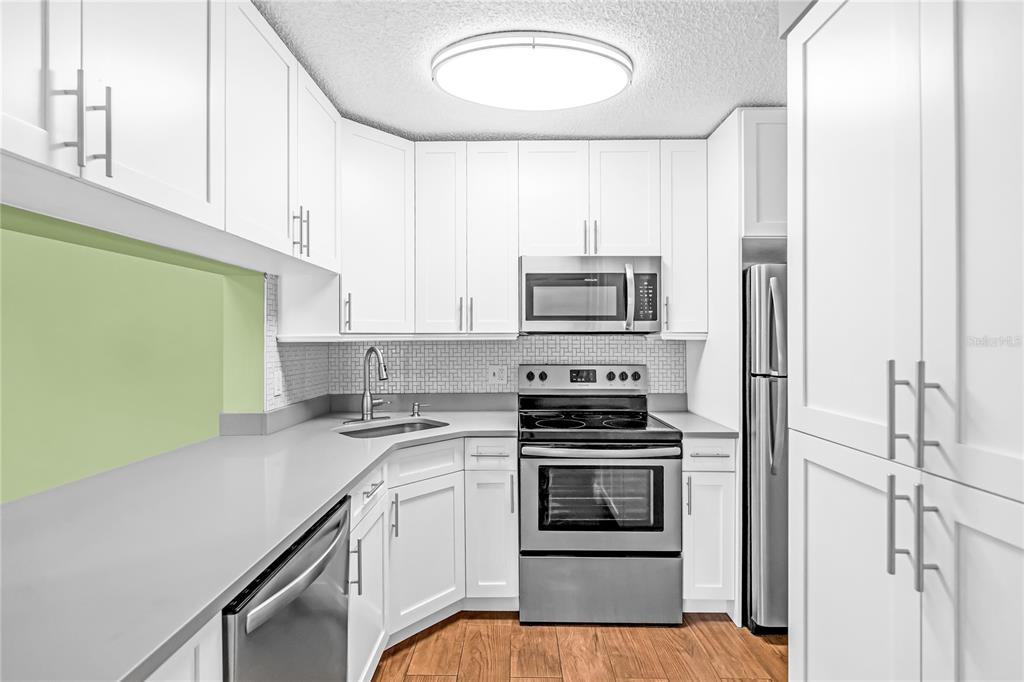 A kitchen features white cabinets, stainless steel appliances, gray countertops, and light wood flooring — 806 SKY PINE WAY UNIT B3, GREEN ACRES, FL