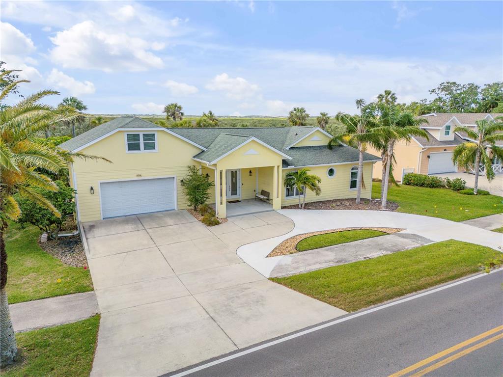 A yellow house with a green roof and a concrete driveway sits beside a road — 1804 SAXON DRIVE, NEW SMYRNA BEACH, FL