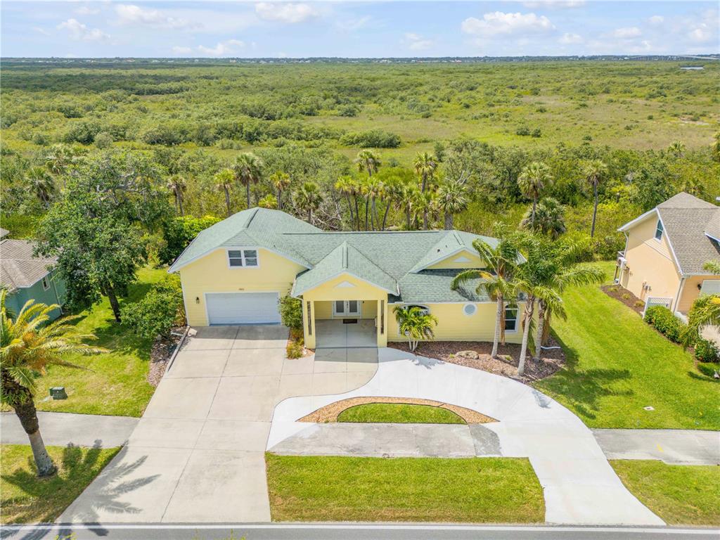 An aerial view of a yellow house with a green roof and a concrete driveway — 1804 SAXON DRIVE, NEW SMYRNA BEACH, FL