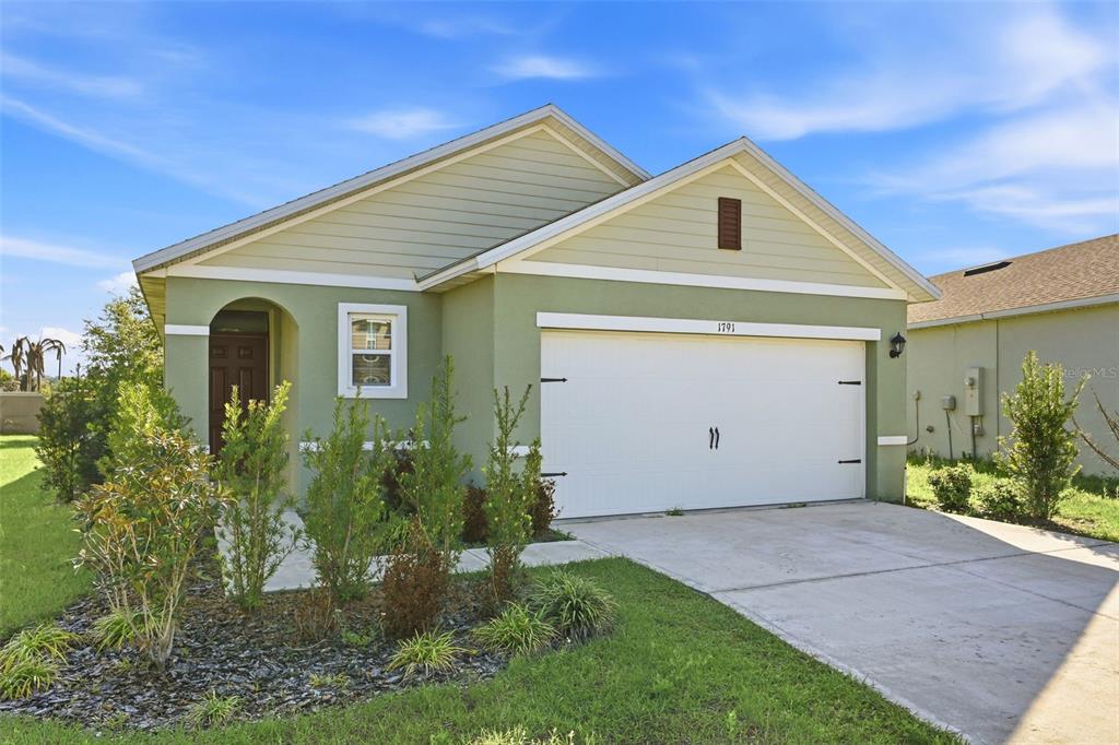 A single-story house with green stucco walls, a white garage door, and a front entrance — 1791 POST OAK DRIVE, DAVENPORT, FL