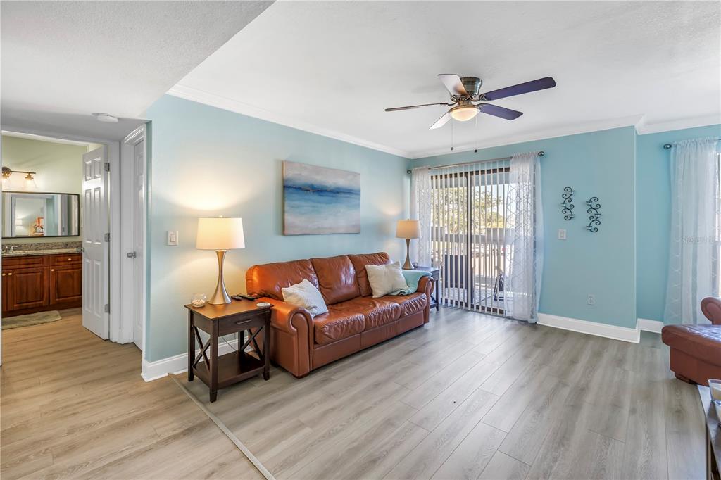 A living room features light blue walls, a brown leather sofa, and wood-look flooring — 455 ALT 19 S UNIT 266, PALM HARBOR, FL