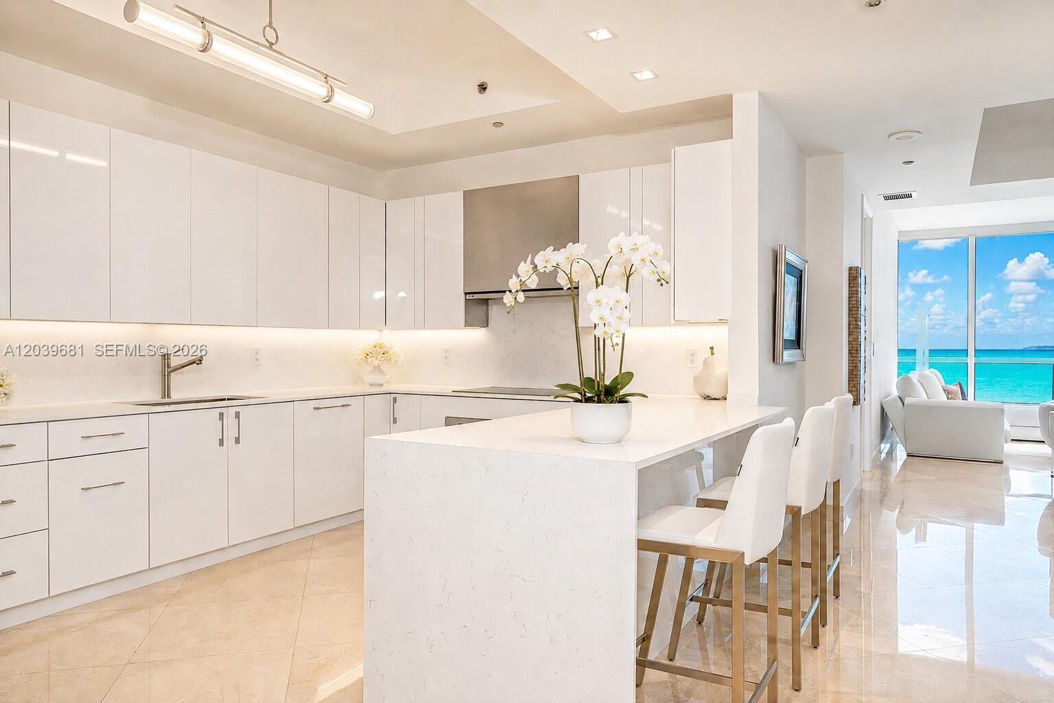 A modern white kitchen features a waterfall island, sleek cabinetry, and an ocean view — 100 S Pointe Dr # 1507, Miami Beach FL 33139, MIAMI BEACH, FL
