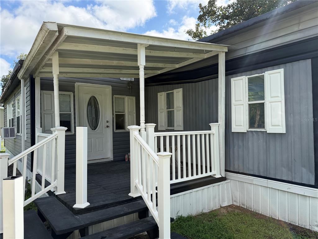 A mobile home exterior features a covered wooden deck with white railings and stairs — 111 SW 158TH TERRACE, OCALA, FL