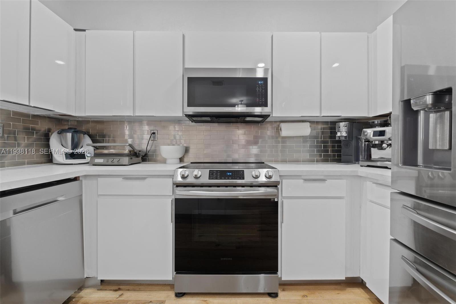 A modern kitchen features white cabinets, stainless steel appliances, and a metallic subway tile backsplash — 3436 W 90th St, Hialeah FL 33018, HIALEAH, FL