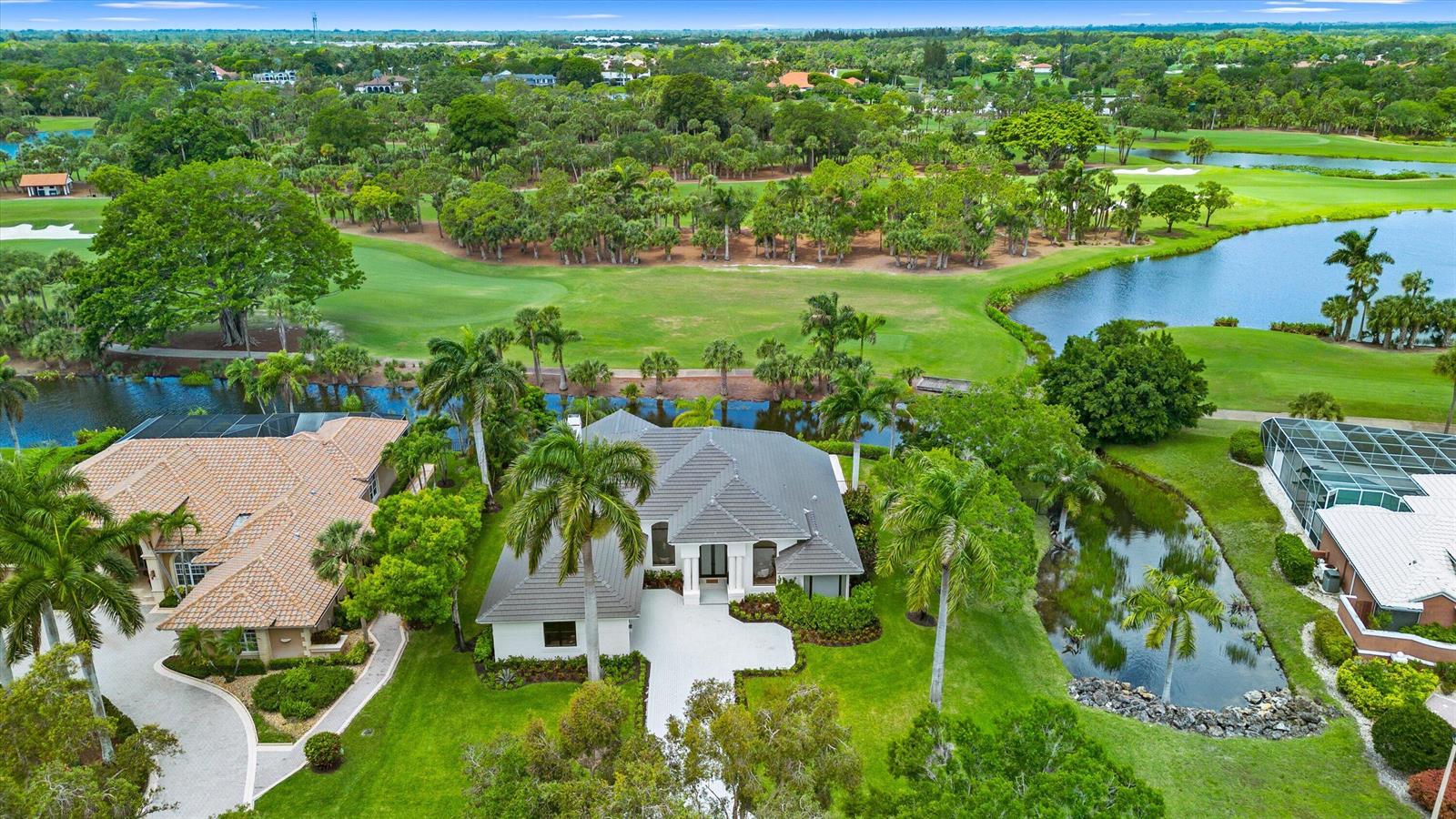 An aerial view shows a house with a gray roof surrounded by lawns and water — 1330 Breakers West Boulevard, West Palm Beach FL 33411, WEST PALM BEACH, FL