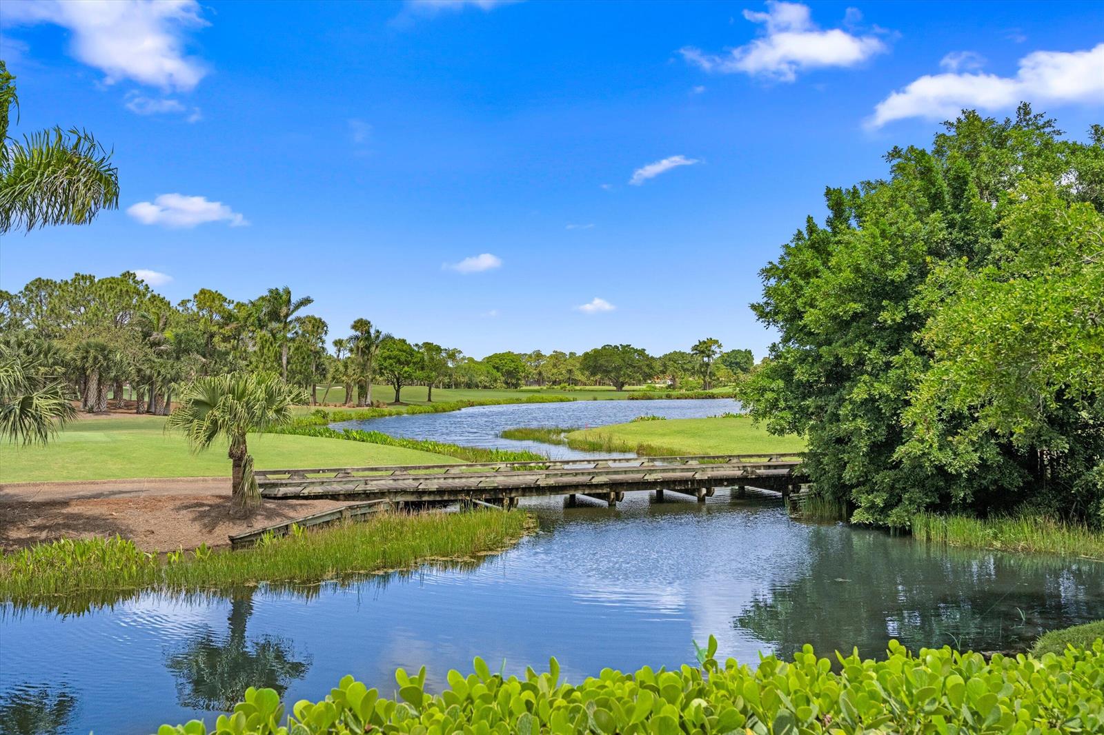 A wooden bridge crosses a narrow waterway on a sunny golf course with lush trees — 1330 Breakers West Boulevard, West Palm Beach FL 33411, WEST PALM BEACH, FL
