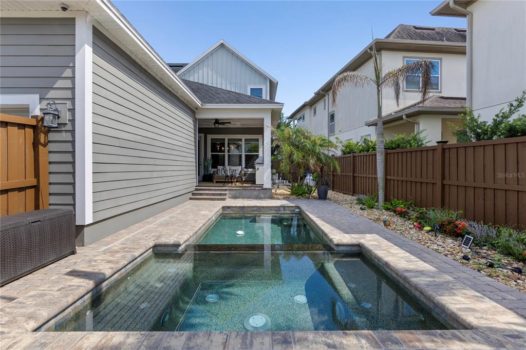 A small rectangular swimming pool sits in a paved backyard next to a gray house — 13041 GABOR AVENUE, ORLANDO, FL