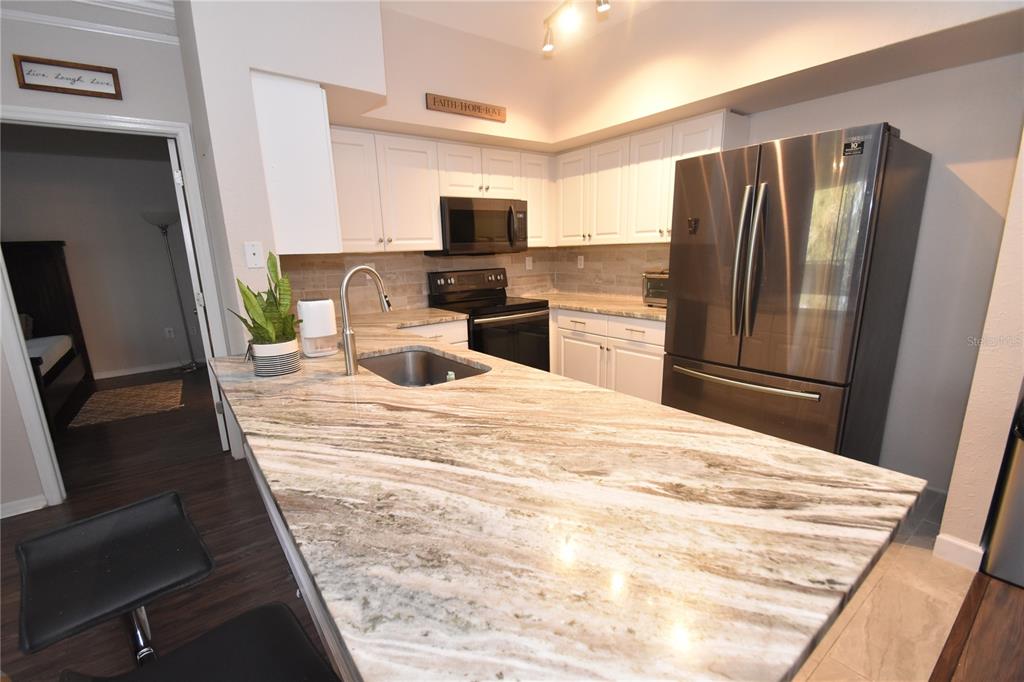 A kitchen features white cabinets, granite countertops, a stainless steel refrigerator, and a center island — 4178 CENTRAL SARASOTA PARKWAY UNIT 324, SARASOTA, FL