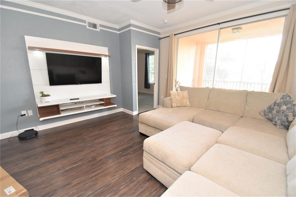 A living room features a wall-mounted television, a large sectional sofa, and wood-look flooring — 4178 CENTRAL SARASOTA PARKWAY UNIT 324, SARASOTA, FL